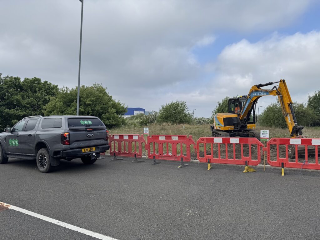 JBB Knotweed Solutions van and JCB carrying out reinstatement works at a roadside commercial site after excavation.